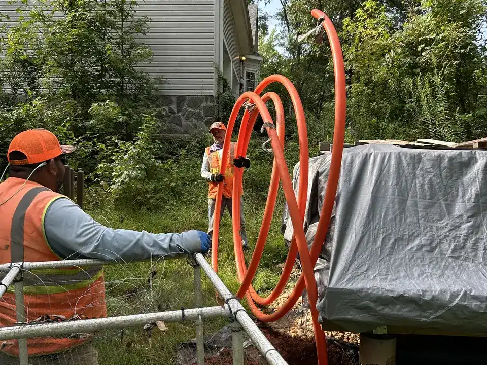 Crew member staging orange HDPE conduit coils and PVC pipe at a Spartanburg County, SC home ahead of pullback