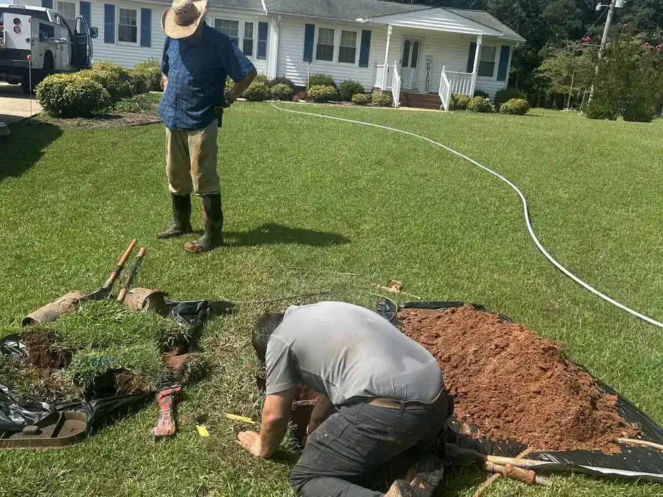 Technician connecting a new water service line at a shallow tie-in pit in an Oconee County, SC front yard while the homeowner looks on