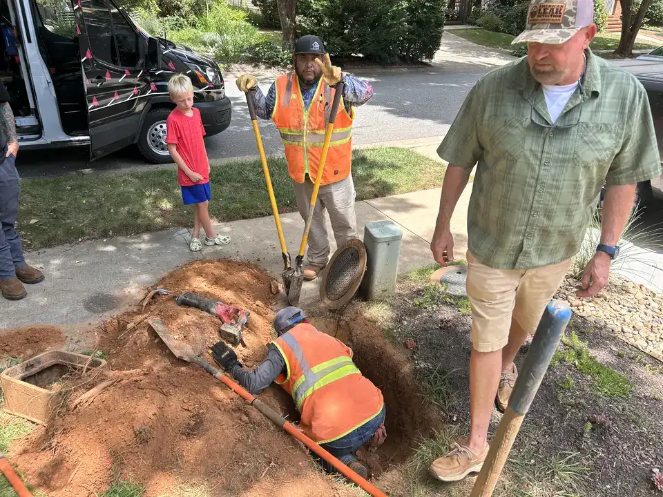 Sloan Underground crew hand-digging a water service tie-in pit at the curb of an Asheville, NC home